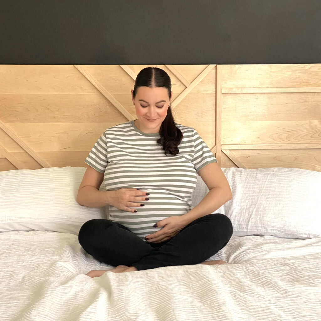 Pregnant woman sitting on bed using pregnancy essentials. 