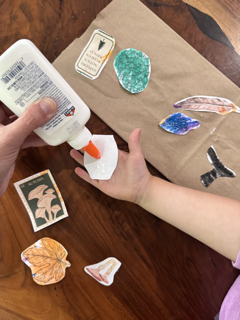 A child gluing colorful cut-out botanical illustrations onto a brown paper bag to make a DIY fall nature treasure bag.